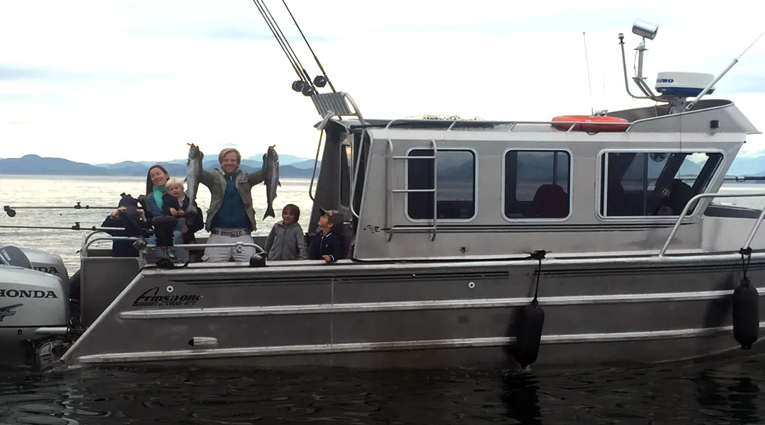 Family holding up 2 freshly caught salmon on the back of our boat